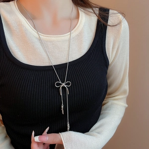 Detail of silver bow pendant necklace with long tassels on a model wearing black and beige