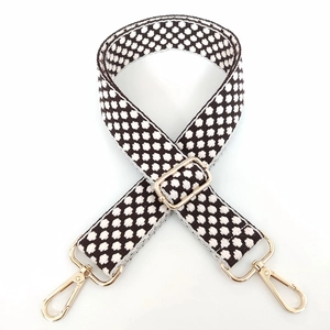 Macro detail of black and white geometric woven strap with gold metal hooks and buckle