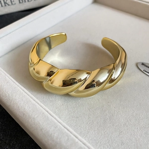 Detail of twisted gold-plated bangle with mirror finish on a grey velvet display case