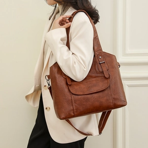 Brown faux leather tote bag with front pocket worn by a model in a beige blazer
