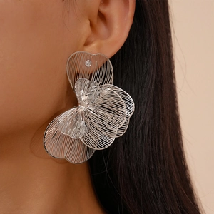 Close-up of a model wearing large silver-toned hollow petal earrings with a metallic finish