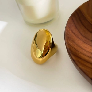 Minimalist gold oval chunky ring on wooden tray with elegant lifestyle background