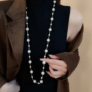 Elegant long faux pearl necklace with gold chain layered over a brown suede jacket