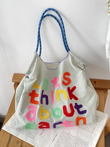 Detail of colorful embroidered text on a casual large canvas tote bag with blue handles