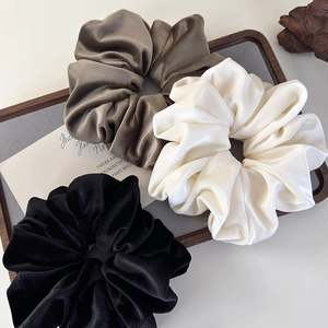 Three premium velvet scrunchies in coffee, cream, and black on a wooden display board