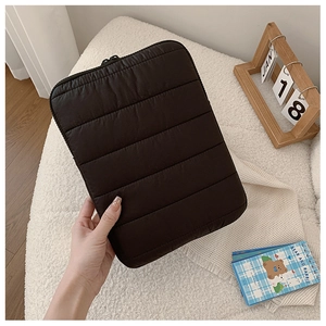 Detail of black quilted laptop sleeve with puffer texture held in a cozy home setting