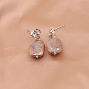 Detailed view of silver rose stud earrings with baroque pearls on champagne silk fabric