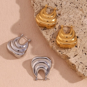 Detailed view of layered U-shaped earrings in gold and silver finish on a stone pedestal