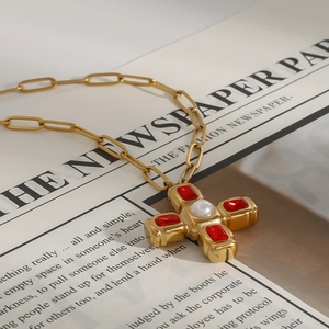 Détail d'un pendentif croix doré avec perles et pierres rouges sur fond de journal