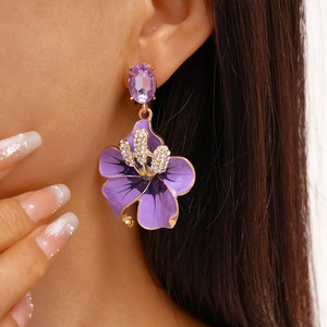 Macro di un orecchino floreale viola con bordo dorato e strass su una modella