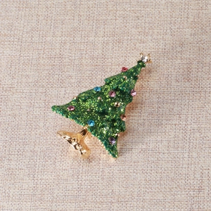 Close-up of green enamel Christmas tree brooch with colorful rhinestones on beige fabric