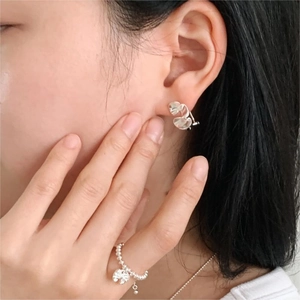 Detail of silver heart stud earrings and beaded ring worn by a model for a minimal look