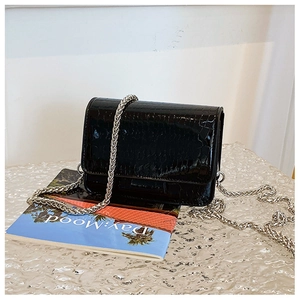 Detail of black faux crocodile leather texture and silver chain on a mini crossbody bag