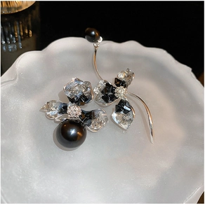 Detail shot of asymmetric floral earrings with black pearls and crystals on a white tray