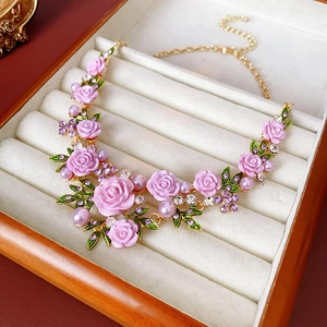 Détail du collier doré avec roses roses, perles mauves et feuilles vertes dans l'écrin