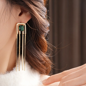 Close-up of gold fringe earrings with square emerald green stones on a model ear