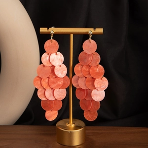 Detail of orange tiered shell tassel earrings hanging on a gold jewelry display stand