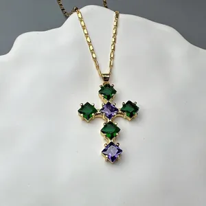 Detailed shot of golden cross pendant with green and purple gemstones on ceramic tray