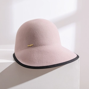Pink wool felt cloche hat with black trim and gold logo on minimalist stone steps