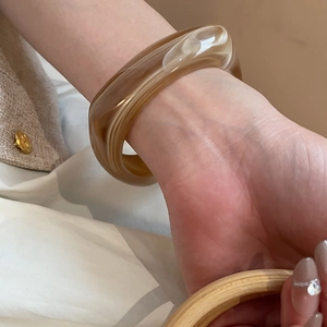 Close-up of wide amber marble resin bangle on wrist with elegant beige tweed jacket