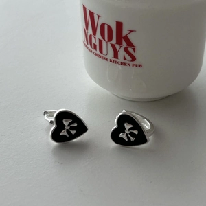 Detail of silver heart hoop earrings with black enamel and bow motif decoration