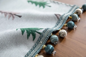Detailed close-up of Christmas table runner with pine tree embroidery and beaded tassels