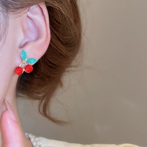 Close-up of cherry stud earring with red gemstones and green leaves on a model
