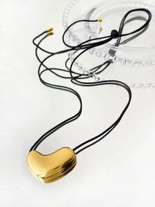 Polished 14K gold heart pendant necklace on adjustable black cord over a glass plate