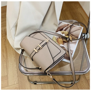 Beige PU leather crossbody bag with metal buckle on acrylic chair in lifestyle setting
