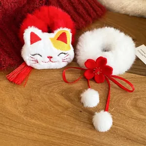 Winter plush Lucky Cat hair scrunchies with white pompoms and red tassels on wood