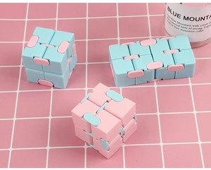 Detailed view of three blue and pink fidget infinity cubes on a pink grid surface
