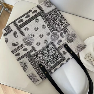 Detail of paisley bandana print tote bag with black leather handles and metal rivets