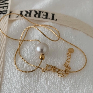 Close-up of pearl pendant with gold chain and heart charm on a soft white background