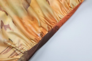 Macro view of pleated satin fabric with orange abstract print and detailed stitching