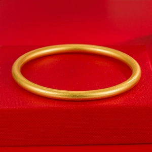 Classic matte gold round bangle bracelet displayed on a premium red jewelry box surface