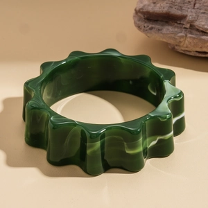 Dettaglio macro del bracciale in acrilico verde scuro a forma di ingranaggio con marmo