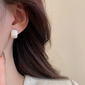 Close-up of elegant gold square earrings with white resin inlay worn on a model ear