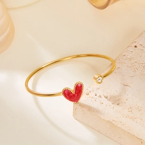 Close-up of golden open bangle with red heart charm and sparkling round zircon detail