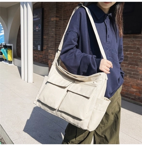 Detail of off-white canvas messenger bag with dual front flap pockets and wide shoulder strap
