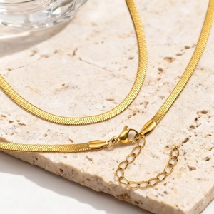Detail of golden snake bone necklace with lobster clasp on beige stone background