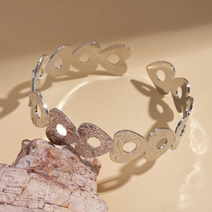 Dettaglio del bracciale rigido in metallo argentato traforato a cuore con finitura martellata