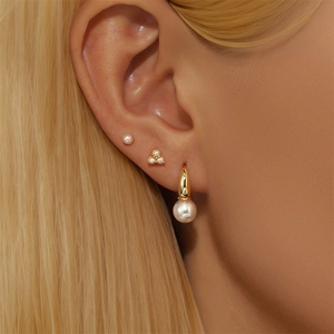 Detailed view of gold pearl stud and hoop earring set worn on ear showing textures