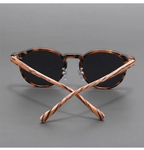 Detail view of retro round tortoiseshell sunglasses with wood-grain temples and dark lenses