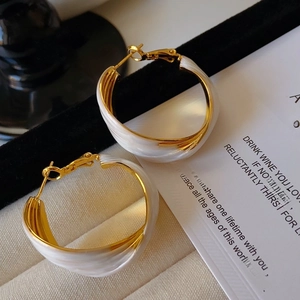 Detailed view of vintage gold U-shaped hoop earrings with white enamel on ribbed fabric