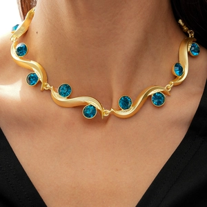 Detail of vintage gold wave necklace featuring circular blue gemstones on model