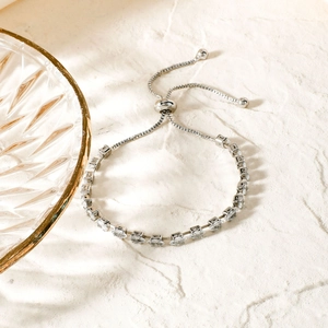 Adjustable silver bracelet with square zircons on beige stone background