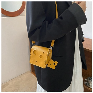Close-up of a mini yellow cheese-shaped crossbody bag with circular holes and a charm