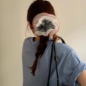 Close-up of black and white plaid scrunchie with red stitching on a braided ponytail