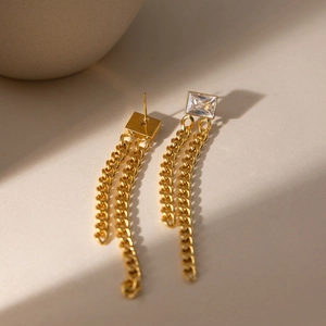 Detail of gold chain tassel earrings with rectangular zircon on warm stone background