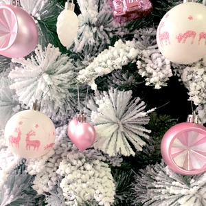 Close-up of pink and white heart-shaped and pinecone Christmas ornaments on snow branches